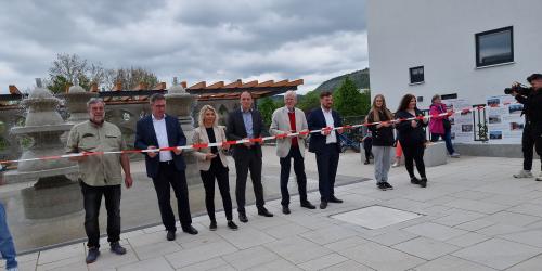 Mehrere Personen schneiden ein Band vor einem Platzmit Brunnen durch