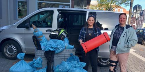 Vor einem grauen Kastenwagen stehen zwei Frauen neben diversen Tüten und KIsten, in denen sich Spenden befinden.