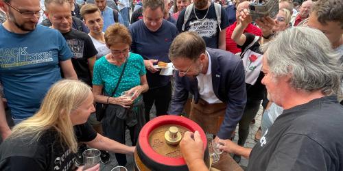 Ein Mann sticht ein Bierfass an, viele Menschen beobachten ihn