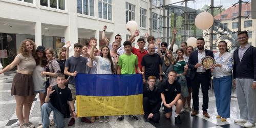 Einen Gruppe von Jugendlichen steht mit ein paar erwachsenen für ein Gruppenfoto zusammen und halten eine Ukraine-Flagge.