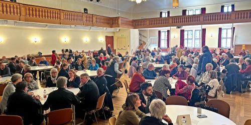 Menschen sitzen an Runden Tischen in einem großen Saal