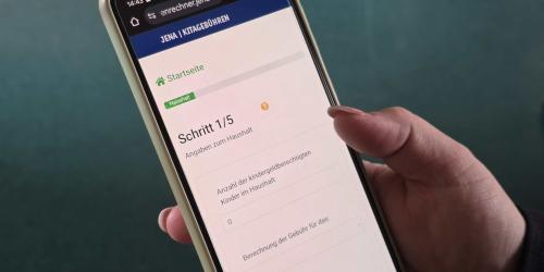 Eine Hand hält ein Smartphone auf dem der Kitagebührenrechner der Stadt Jena geöffnet ist.