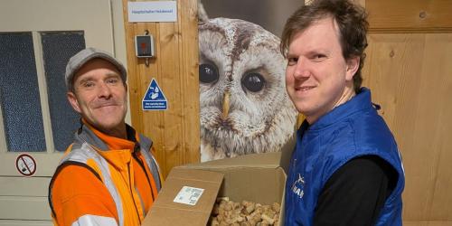 Zwei Männer halten eine Umzugskiste, die gefüllt ist mit Korken.