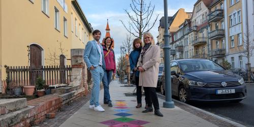 Ein Mann und drei Frauen stehen an einem bunten Hüpfekästchen.
