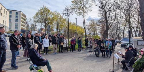 Mehrere dutzend Personen stehen und sitzen im Halbkreis um eine Musikgruppe.