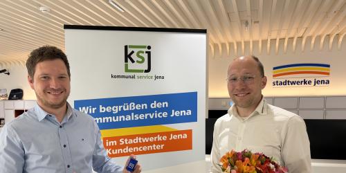 Zwei Männer stehen nebeneinander. Der eine hat einen Blumenstrauß in der Hand.