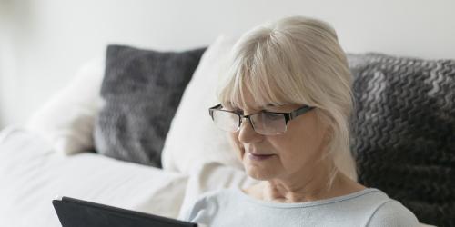Seniorin sitzt auf einer Couch und surft mit einem Tablet