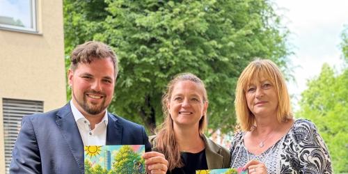 Ein Mann und zwei Frauen halten einen Flyer in die Kamera
