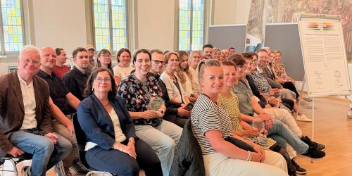 Viele Menschen in einem Raum und alle schauen in die Kamera