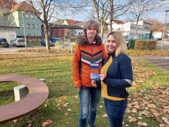  Dörthe Thiele (l.) und Kathrin Bajohr vom Büro für Migration und Integration stehen auf der Wiese vor dem Verwaltungsgebäude am Anger 15 und halten einen Flyer der Antidiskriminierungsstelle in der Hand.