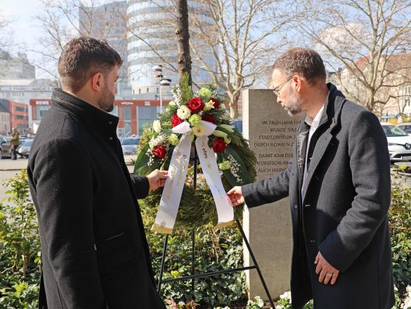 Zwei Personen stehen an einem Gedenkkranz