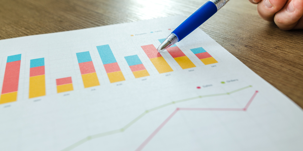 Säulendiagramm auf einem Blatt Papier, das auf einem Tisch liegt. Ein Mensch zeigt mit einem Stift darauf.