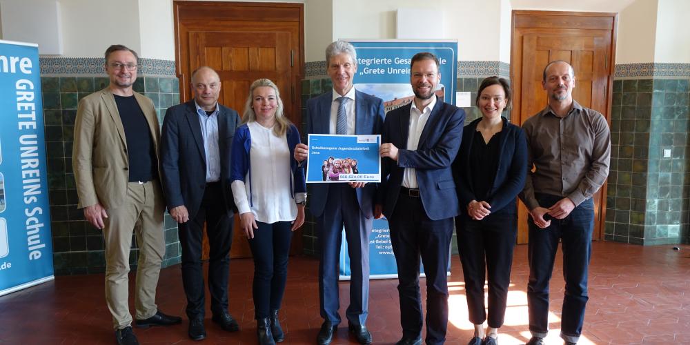 Torsten Wolf (MdL), Dezernent Eberhard Hertzsch (MdL), Schulsozialarbeiterin Andrea Hempel, Minister Helmut Holter, OB Thomas Nitzsche, Jugendhilfeplanerin Nicole Warthemann und Matthias Kehl stehen nebeneinander. Der Minister und der OB halten den Bescheid fest.