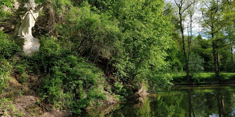 Auf einem Hang an einem Teich steht eine Statue.