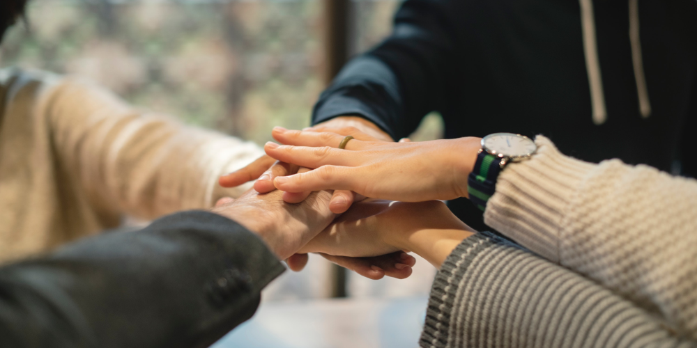 Mehrere Personen legen jeweils eine ihrer Hände übereinander