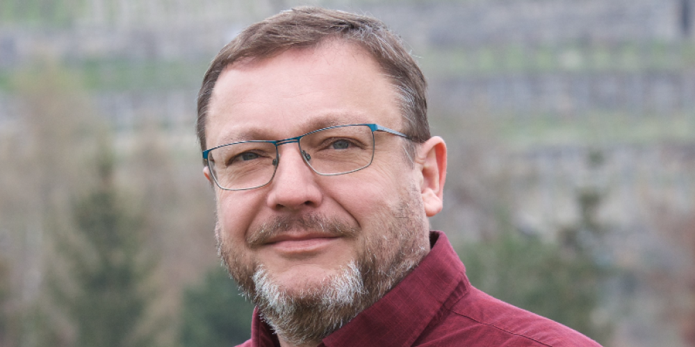 Ein Mann schaut in die Kamera, im Hintergrund Berge