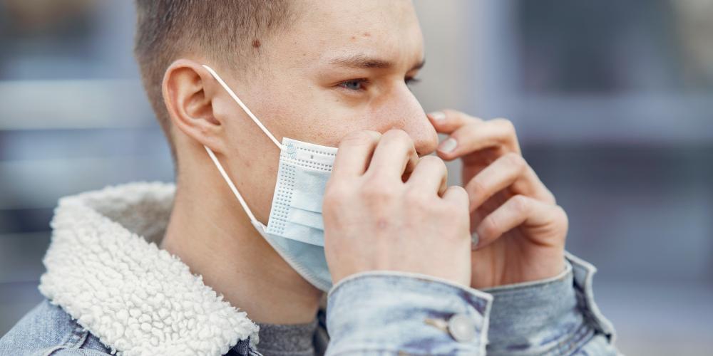 Junger Mann setzt Mund-Nasen-Bedeckung im Freien ab