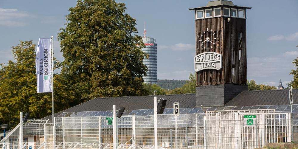 Eine leere Tribüne des Stadions mit dem Jentower im Hintergrund
