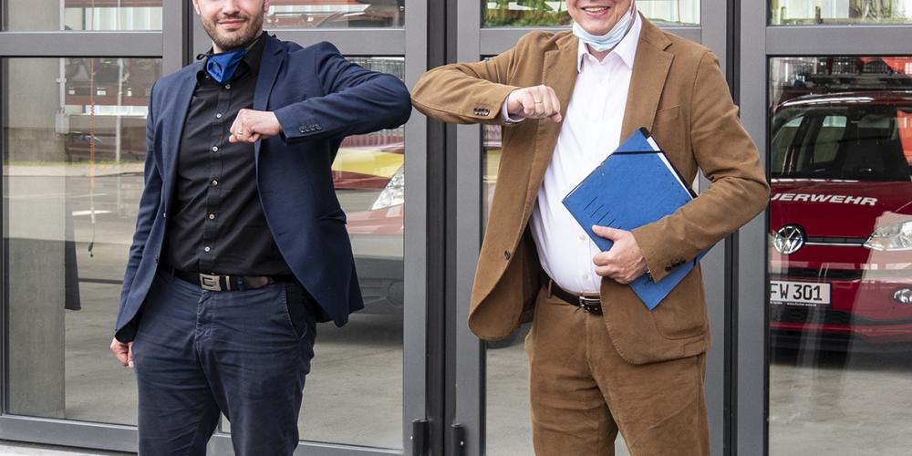 Zwei Männer vor einer Garage stoßen die Ellenbogen zusammen