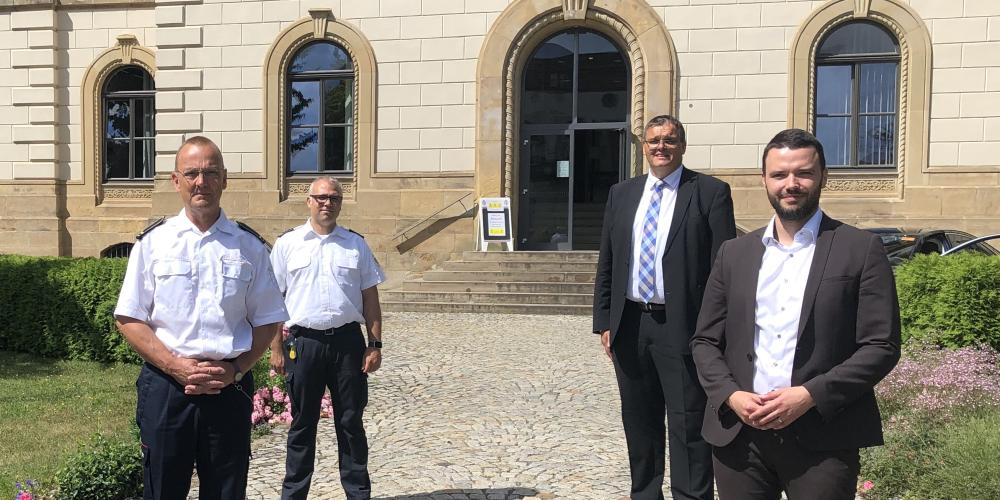 Vier Personen stehen vor einem Haus im Abstand von 1,5 m.