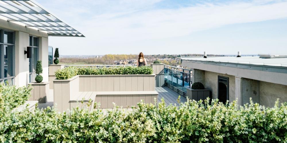 Blick über eine grüne Terasse, im Hintergund eine Landschaft mit Gebäuden