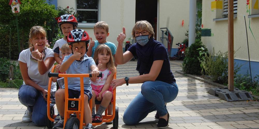 Kinder und Erzieher freuen sich über das neue Dreirad. einige Kinder sitzen schon drauf.