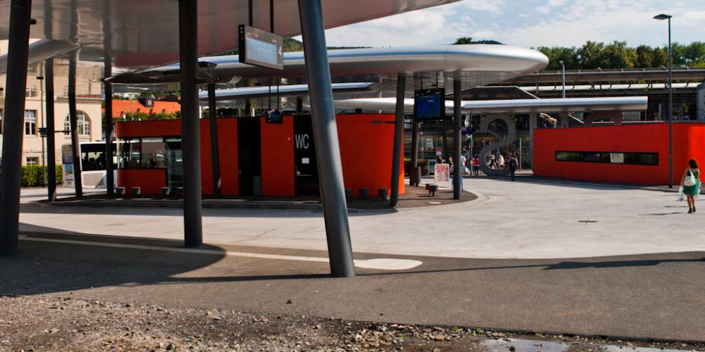 Eine Außenfläche mit einem überdachten Bereich und roten Gebäuden im Hintergrund