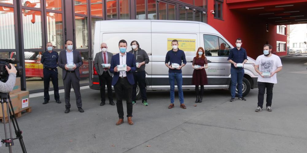 Viele Menschen vor einem Fahrzeug, alle tragen eine Maske