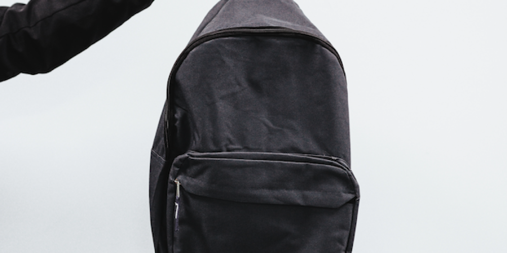 Eine Hand hält einen Rucksack in die Luft