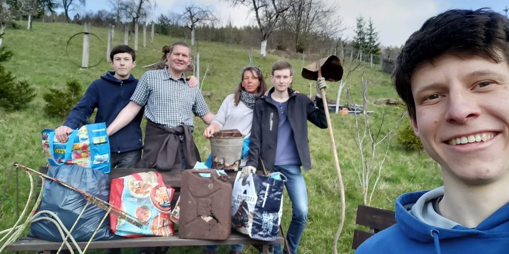 Fünf Menschen stehen auf einer Wiese und halten Müllgegenstände in die Kamera