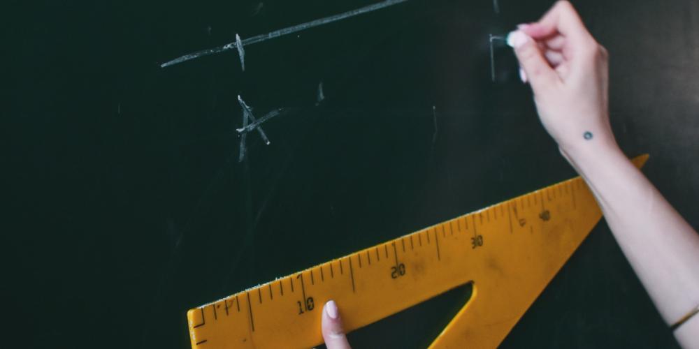 Zwei Hände halten ein Dreieck und schreiben eine geometrische Formel an die Tafel 