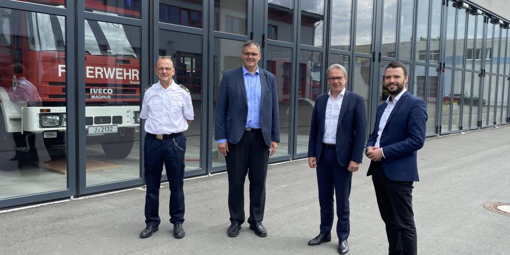 Vier Männer schauen in die Kamera, im Hintergrund ein Feuerwehrgebäude