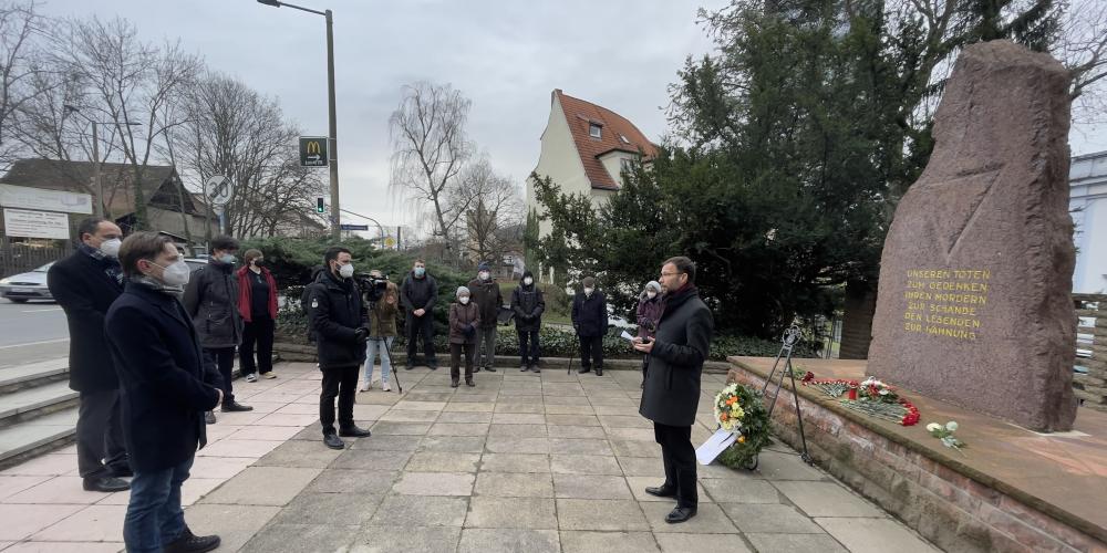 Menschen stehen vor einem Gedenkstein, ein Redner im Vordergrund