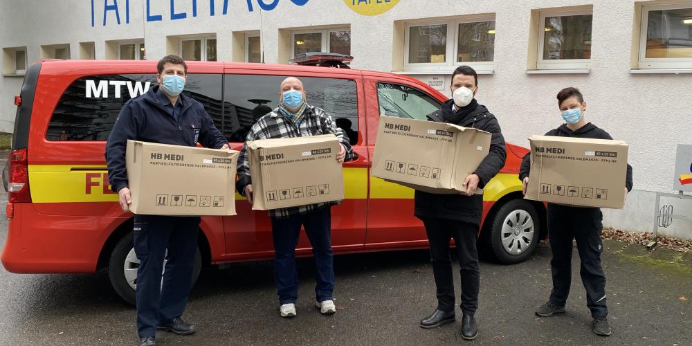 Vier Menschen mit Kisten vor einem Transporter der Feuerwehr