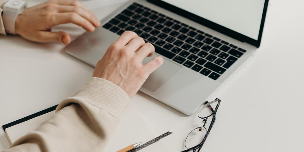 Laptop steht auf dem Tisch man sieht zwei Hände die auf de Tastatur etwas eingeben