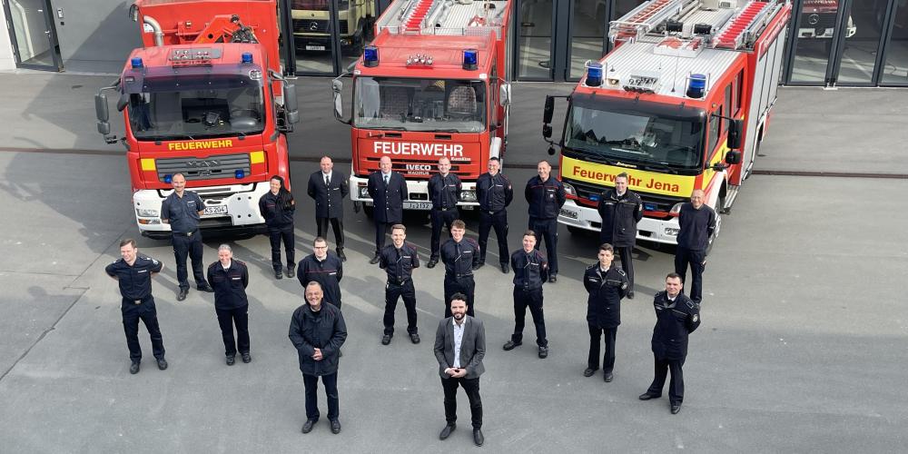 Feuerwehrleute in Uniform vor drei Feuerwehrfahrzeugen