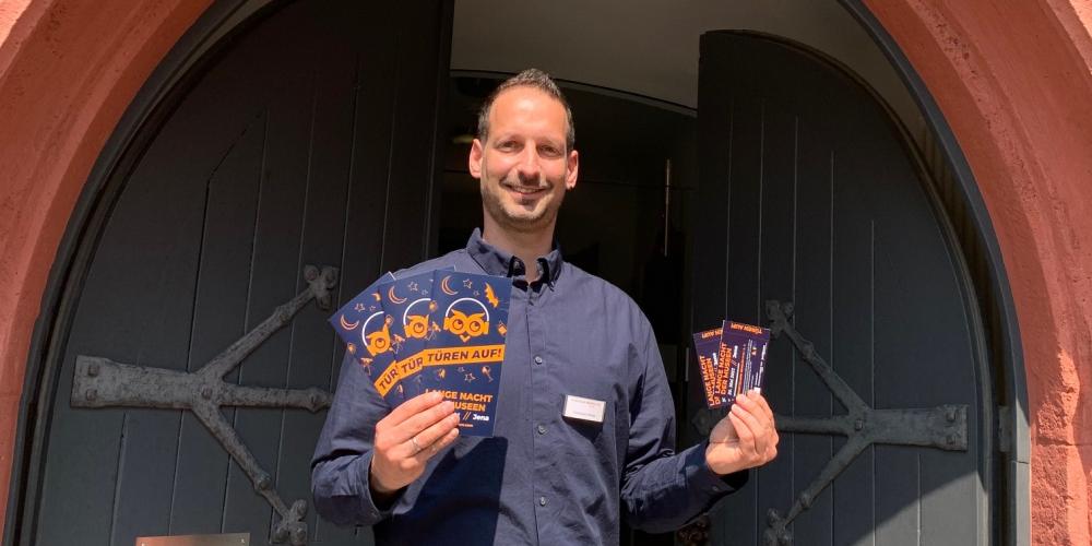 Christian Möller von den Städtischen Museen Jena steht vor einem Tor und hät Tickets in die Kamera.