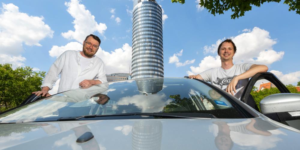 Zwei Männer und ein Auto, im Hintergrund der Jentower