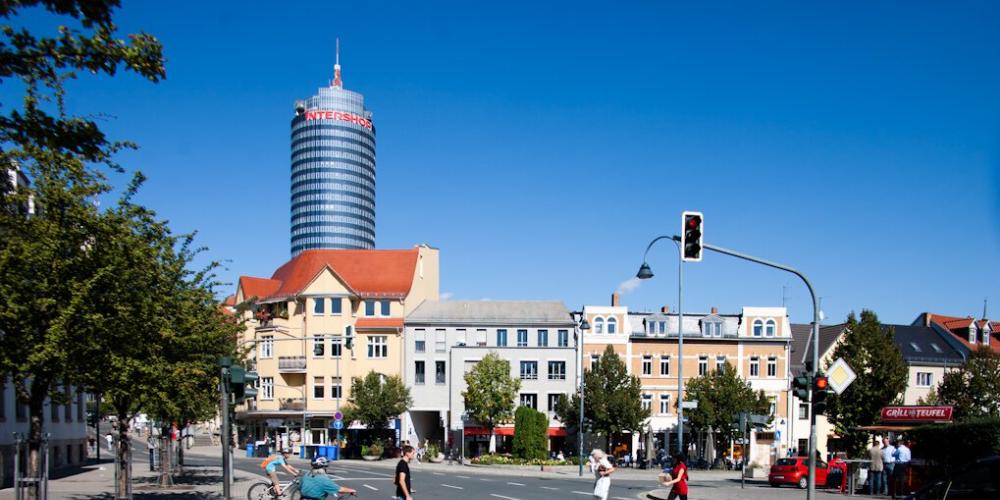 Menschen überqueren eine Straße an einer Ampelkreuzung, im Hintergrund ein großer Turm.