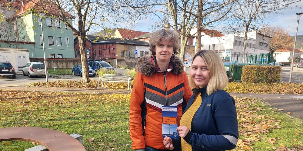  Dörthe Thiele (l.) und Kathrin Bajohr vom Büro für Migration und Integration stehen auf der Wiese vor dem Verwaltungsgebäude am Anger 15 und halten einen Flyer der Antidiskriminierungsstelle in der Hand.