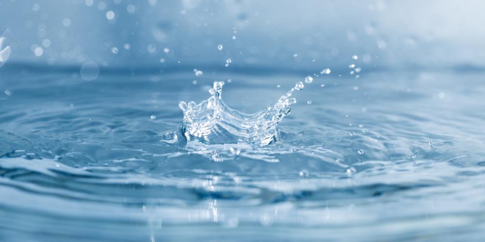 Ein Wassertropfen fällt in ein Glas Wasser. Wassertropfen spritzen weg.