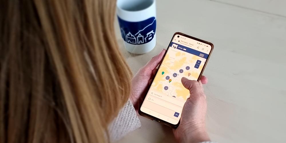 Eine Frau schaut sich am Smartphone die Wandelkarte Jena an.