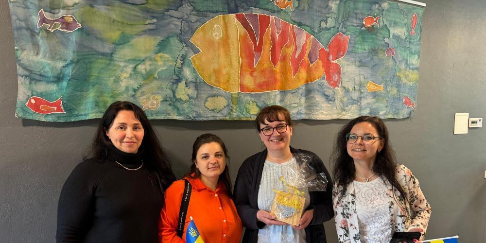 Vier Frauen stehen vor einem Gemälde im Christlichen Gymnasium in Jena und halten Geschenke und ukrainischen Fahnen in den Händen.