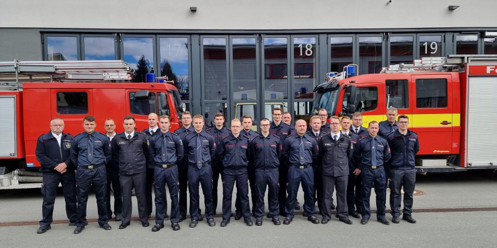 Brandmeisteranwärter stehen auf dem Hof des Gefahrenabwehrzentrums, hinter ihnen stehen zwei Feuerwehrautos