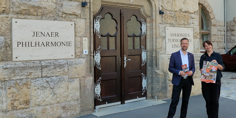 Oberbürgermeister Thomas Nitzsche und Elke Zimmermann, Teamleiterin Denkmalschutz der Stadt Jena, stehen vor dem Eingang des Volkshauses Jena  und halten einen Flyer bzw. ein Plakat des Denkmaltages 2024.