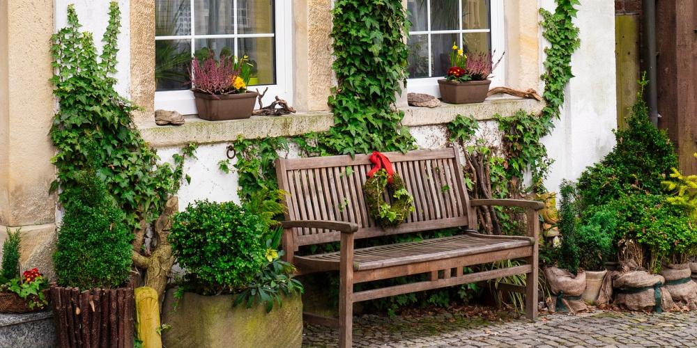 Eine Gartenbank steht vor einem Haus. Pflanzkübel stehen auf beiden Seiten der Bank.