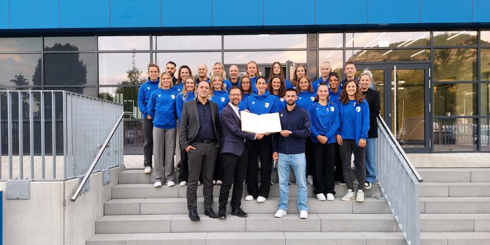 Menschen stehen auf einer Treppe, im Hintergrund ist das Stadion, zwei Personen halten das Goldene Buch der Stadt Jena aufgeklappt