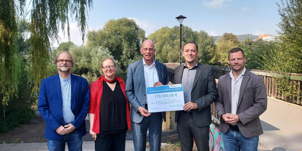 Fünf Personen stehen an der Griesbrücke in Jena. Ein Scheck wird von zwei Personen in der Hand gehalten