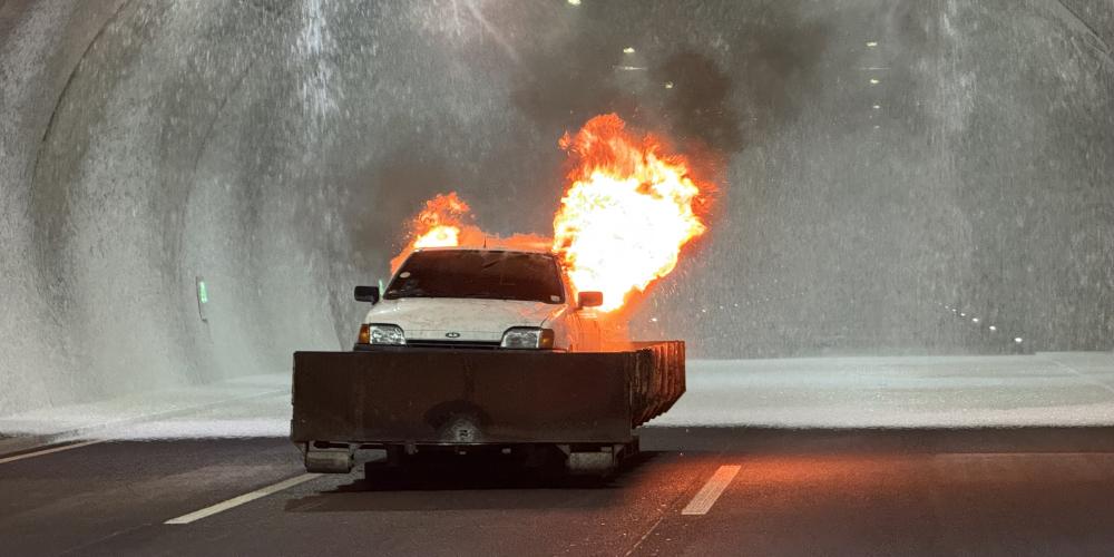 Ein Auto steht im Tunnel und brennt. Die Brandbekämpungsanlage versprüht Löschschaum.