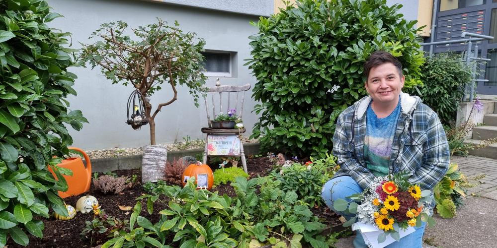 Preisträgerin Kathy Witte hockt neben einem Blumenbeet, welches zu der Grünen Oase gehört, die sie geschaffen hat.